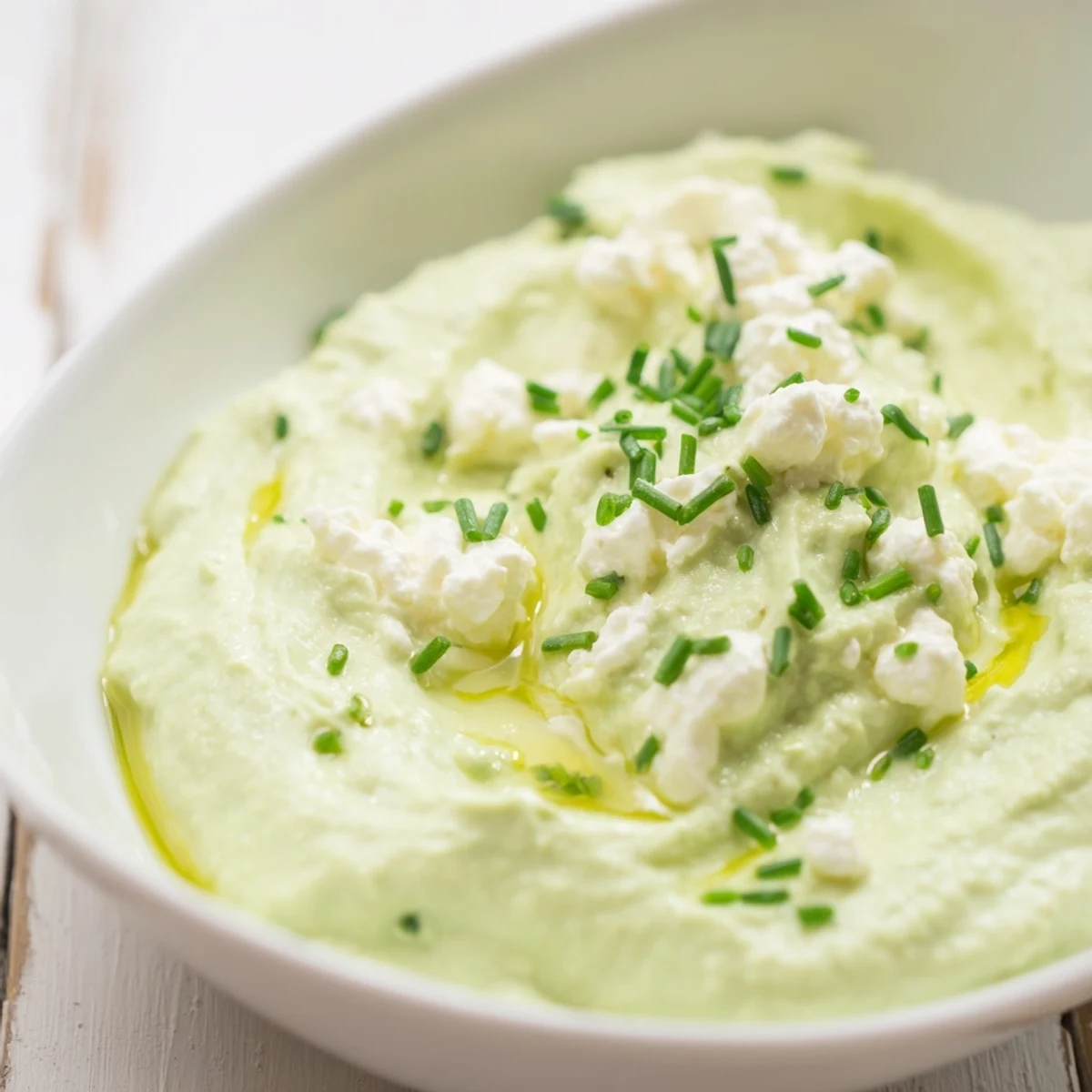 Fresh homemade avocado cottage cheese dip with hints of chives, served elegantly in a bowl.