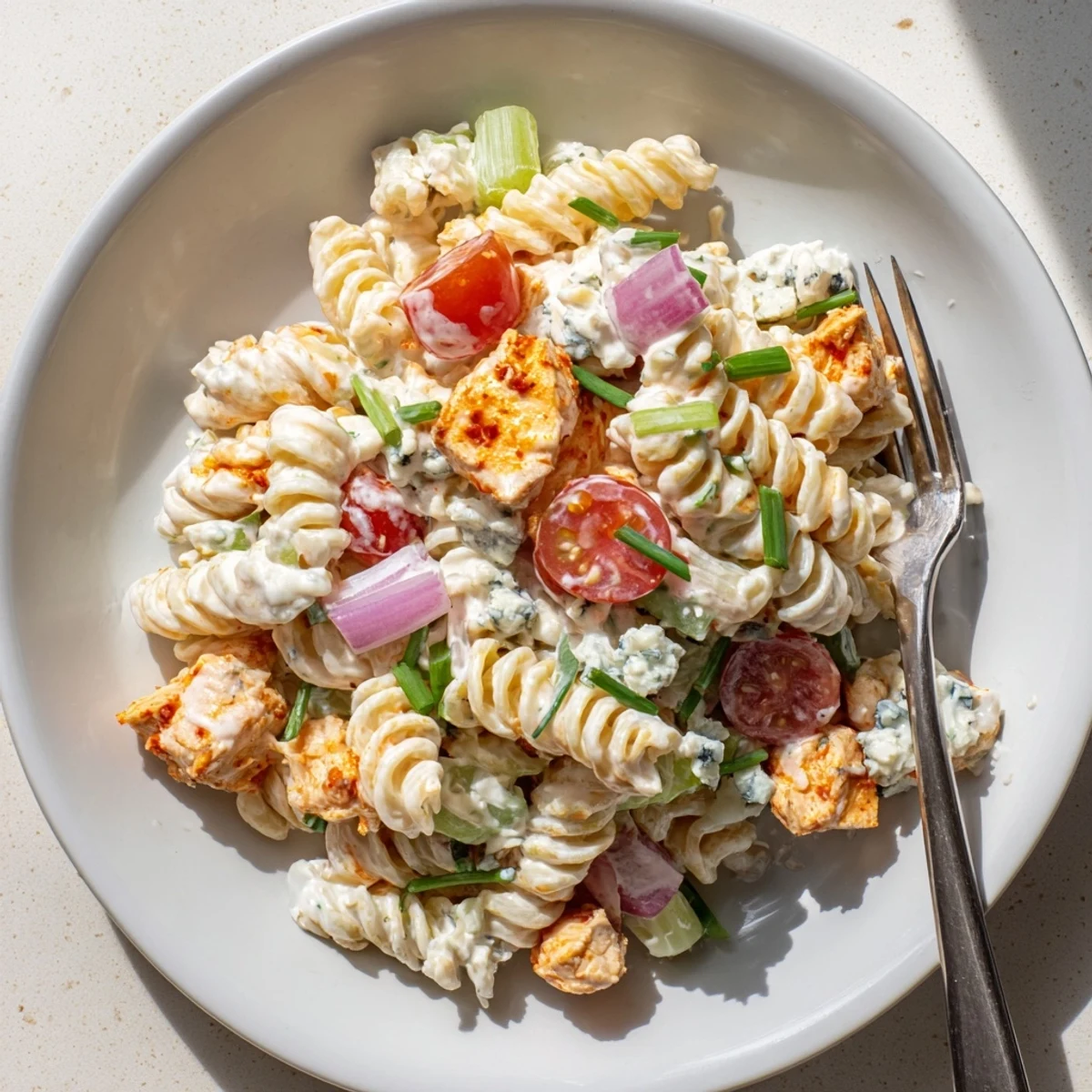 Overhead view of a colorful buffalo chicken pasta salad with blue cheese crumbles and fresh parsley, perfect for a summer potluck.