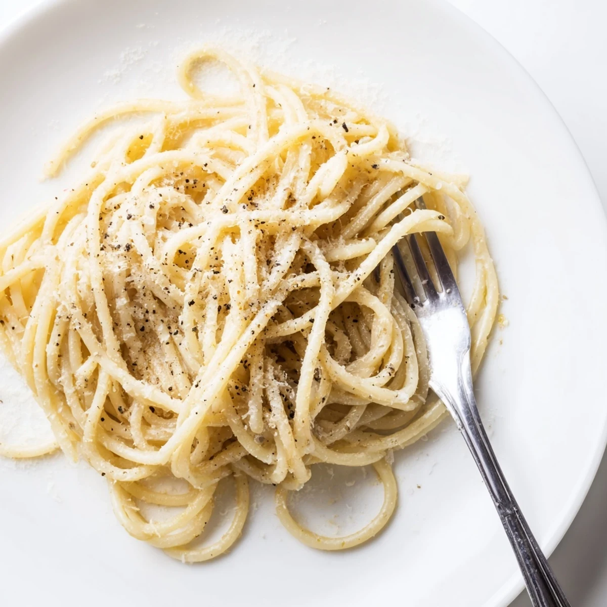 A close-up of Spaghetti Cacio e Pepe in a white bowl, garnished with grated Pecorino and coarse pepper, served ready to eat.
