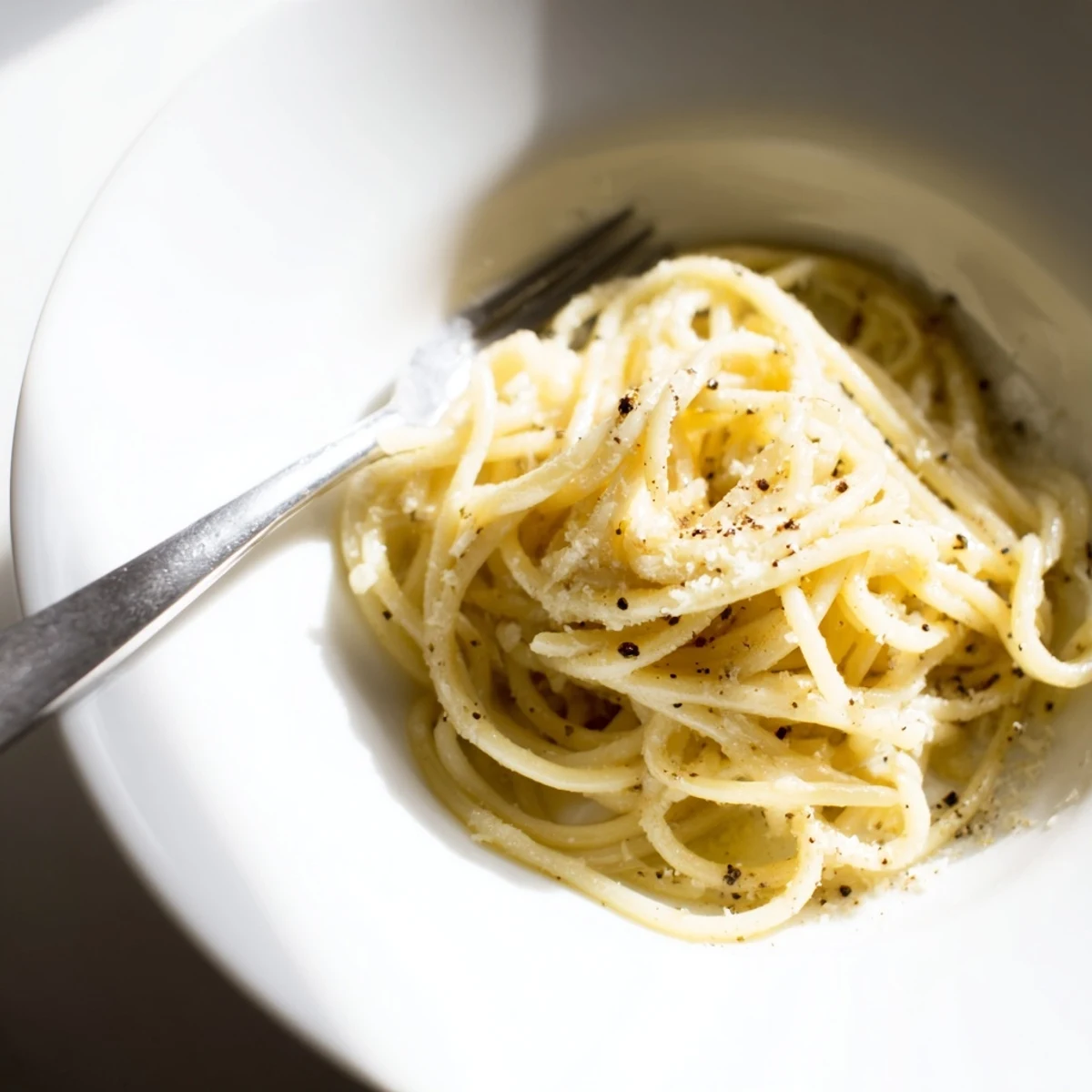 Steaming strands of spaghetti in a skillet, coated in creamy Pecorino Romano and freshly cracked black pepper, a classic Spaghetti Cacio e Pepe.