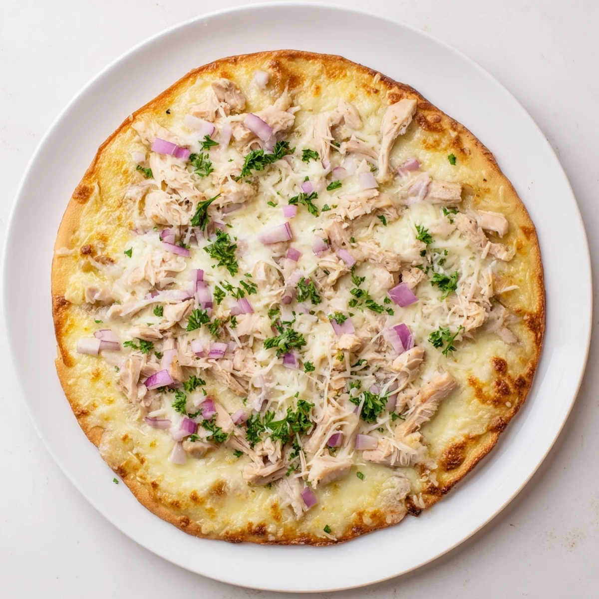 A slice of Chicken Alfredo Pizza rests on a plate, showcasing a golden crust, creamy sauce, and tender chicken pieces.
