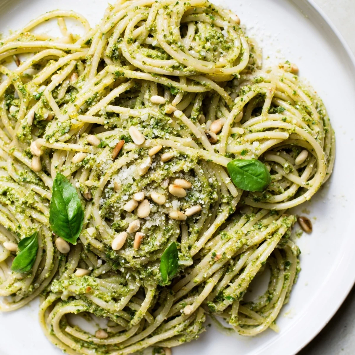 A close-up of Creamy Sunflower Seed Pesto Pasta reveals glossy strands of pasta glistening with olive oil, flecked with toasted sunflower seeds and fresh basil.  