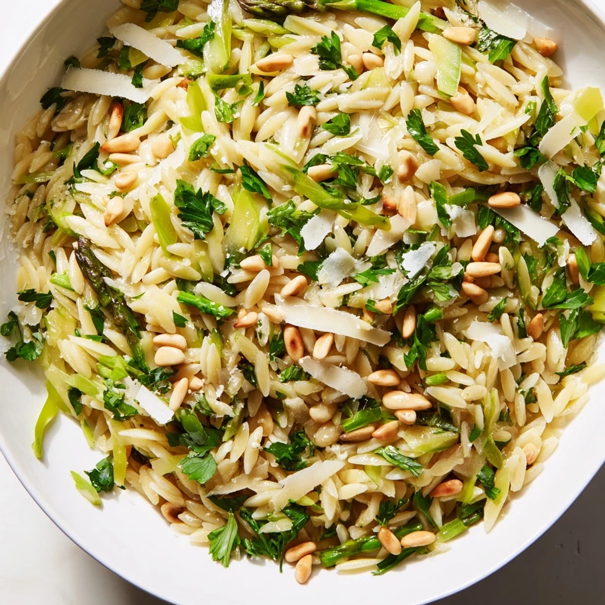 In a white bowl, the Asparagus Lemon Orzo Salad shows bright greens and creamy cheese, ready for a spring picnic or easy vegetarian lunch.