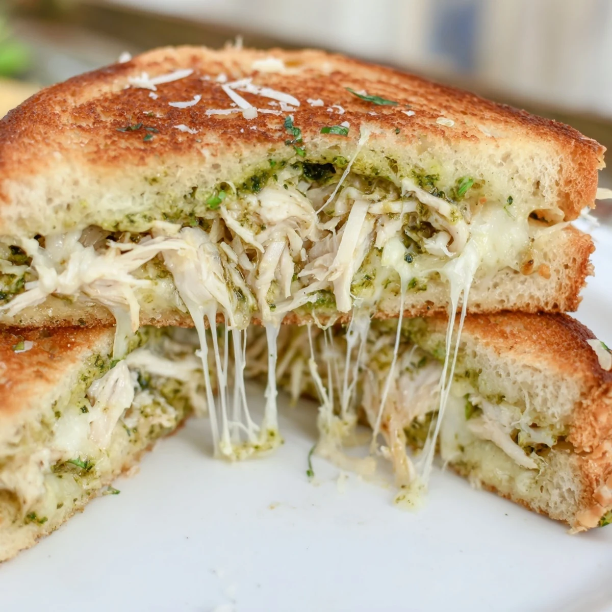 A freshly made Mozzarella Pesto Chicken Grilled Cheese on a wooden cutting board, featuring toasted sourdough bread and vibrant green pesto spread.