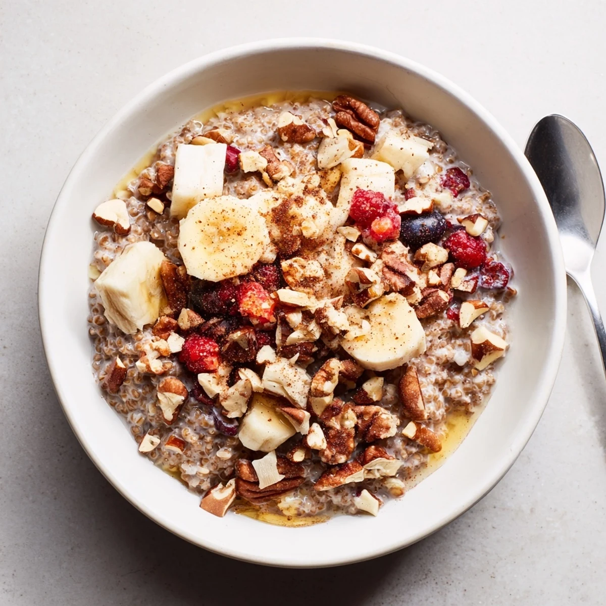 Gluten-free buckwheat groats breakfast with sliced banana, berries, and toasted nuts, drizzled with maple syrup for a sweet start.