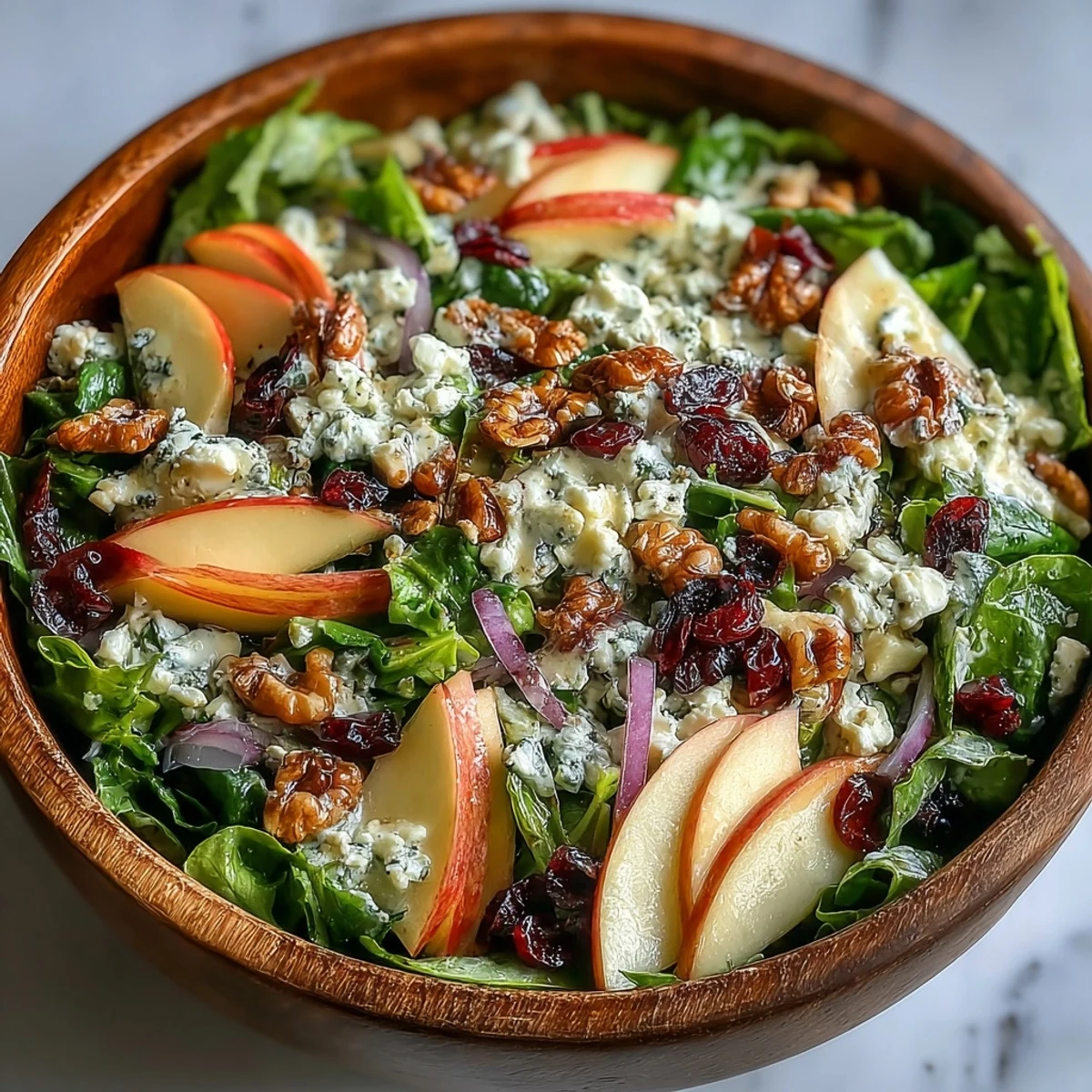 Overhead view of a Mixed Greens and Apple Salad bowl with vibrant greens, red onion, dried cranberries, and walnuts drizzled with dressing.