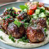 Close-up of spiced venison meatballs served over colorful salad with a side of smooth hummus.  