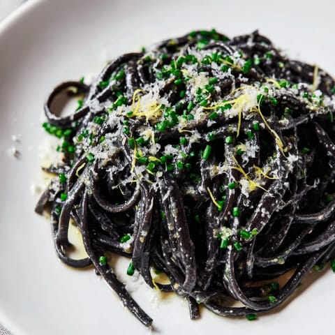 Elegant Squid Ink Pasta with creamy white wine sauce, topped with grated Parmesan and fresh chives on a dark plate.