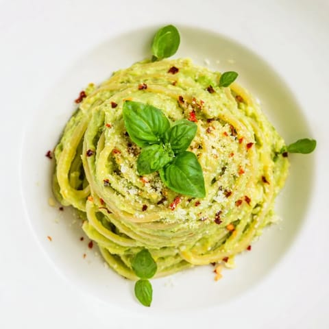 Vibrant green avocado pasta in a white bowl with chili flakes and Parmesan.  