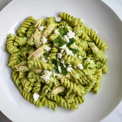 Bright bowl of Cilantro Lime Chicken Pasta garnished with crumbled feta, fresh cilantro, and lime wedges on a rustic table. 