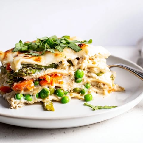A golden baked slice of Spring Veggie Alfredo Lasagna, revealing creamy layers of ricotta, tender asparagus, and vibrant carrots in a 9x13 dish.
