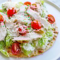 A close-up of Caesar Chicken Flatbread with juicy grilled chicken, crisp romaine, and creamy Parmesan topping.