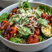 Bright cherry tomatoes and zucchini roast alongside red bell pepper on a baking sheet, ready for an Arugula Pesto Bowl.